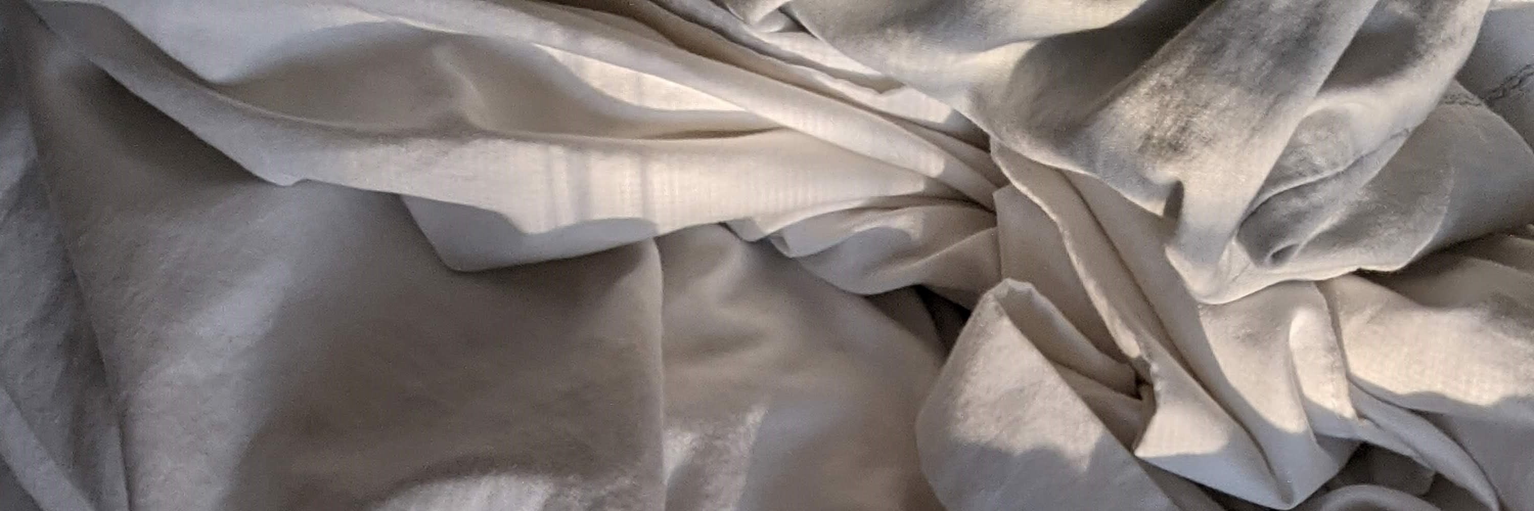 Photo of sun-warmed, rumpled sheets by Susan Wilkinson, 2020. Smells like sweetgrass, patchouli, rose, violet, bergamot blossom, and amber.