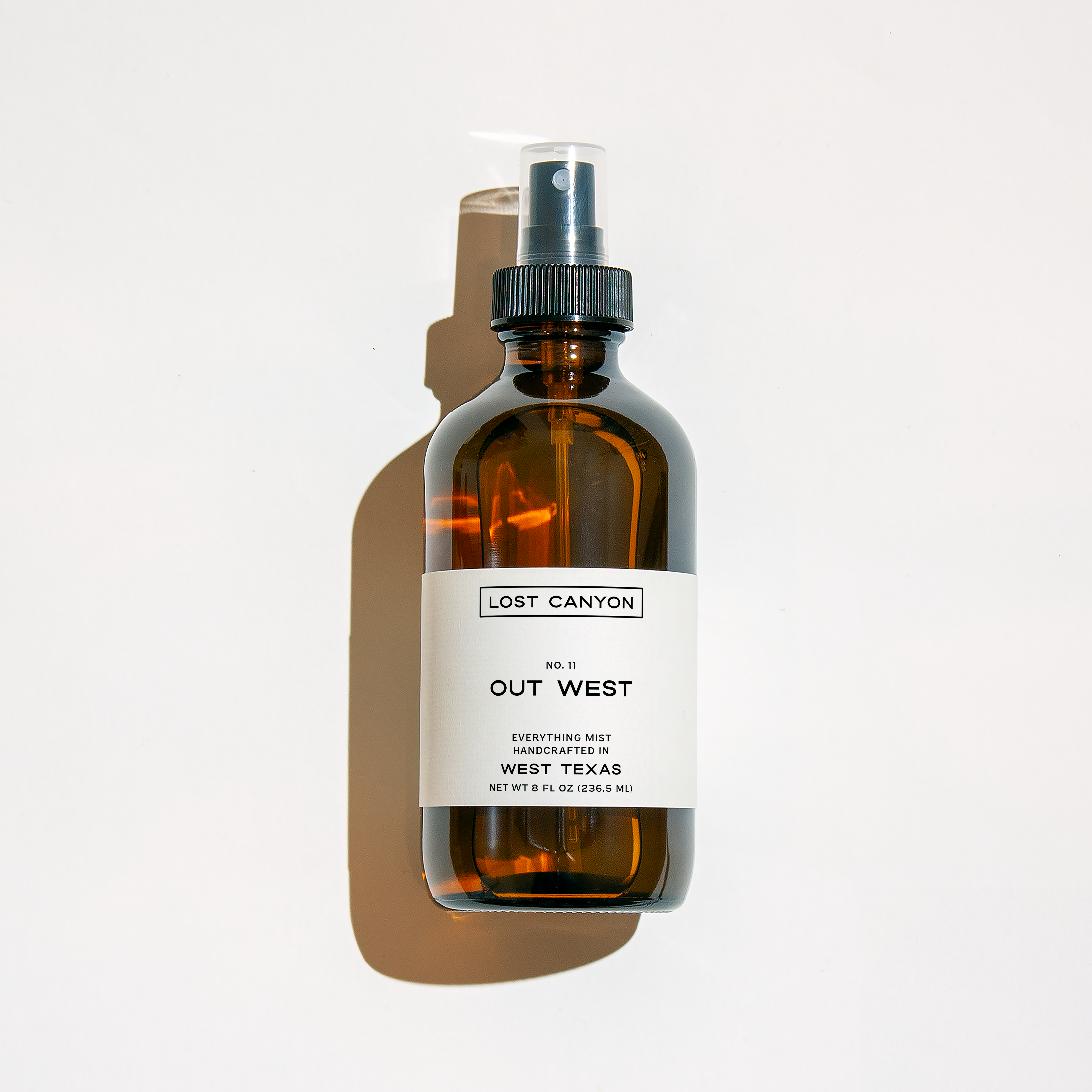 A spray bottle labeled 'OUT WEST' by Lost Canyon, a water-based, skin-safe fragrance with desert-themed notes such as yerba santa, leather, and dry cedar. 
